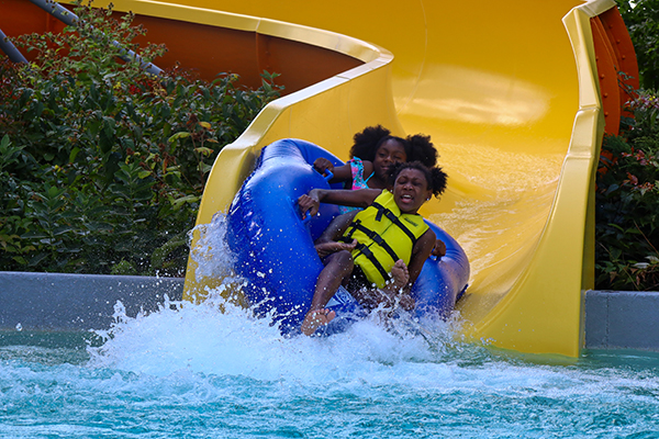 At David F Schulz Aquatic Center, two young girls going down the tube slide are about to make a big splash. The girl in the front of the tube looks a bit scared, while the girl in back is smiling.